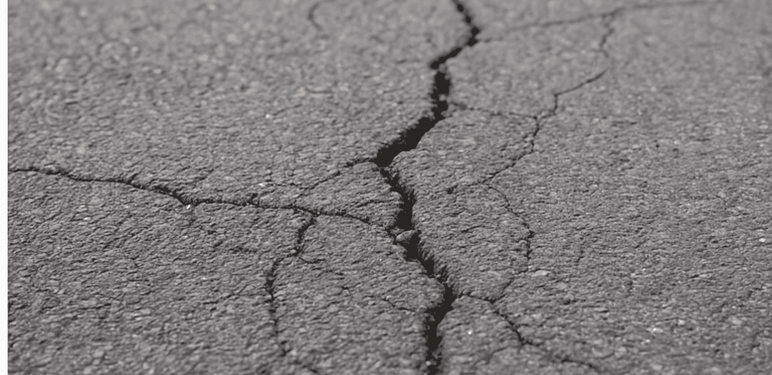 Close-up view of a deep asphalt driveway crack, showing surface deterioration and widening damage.