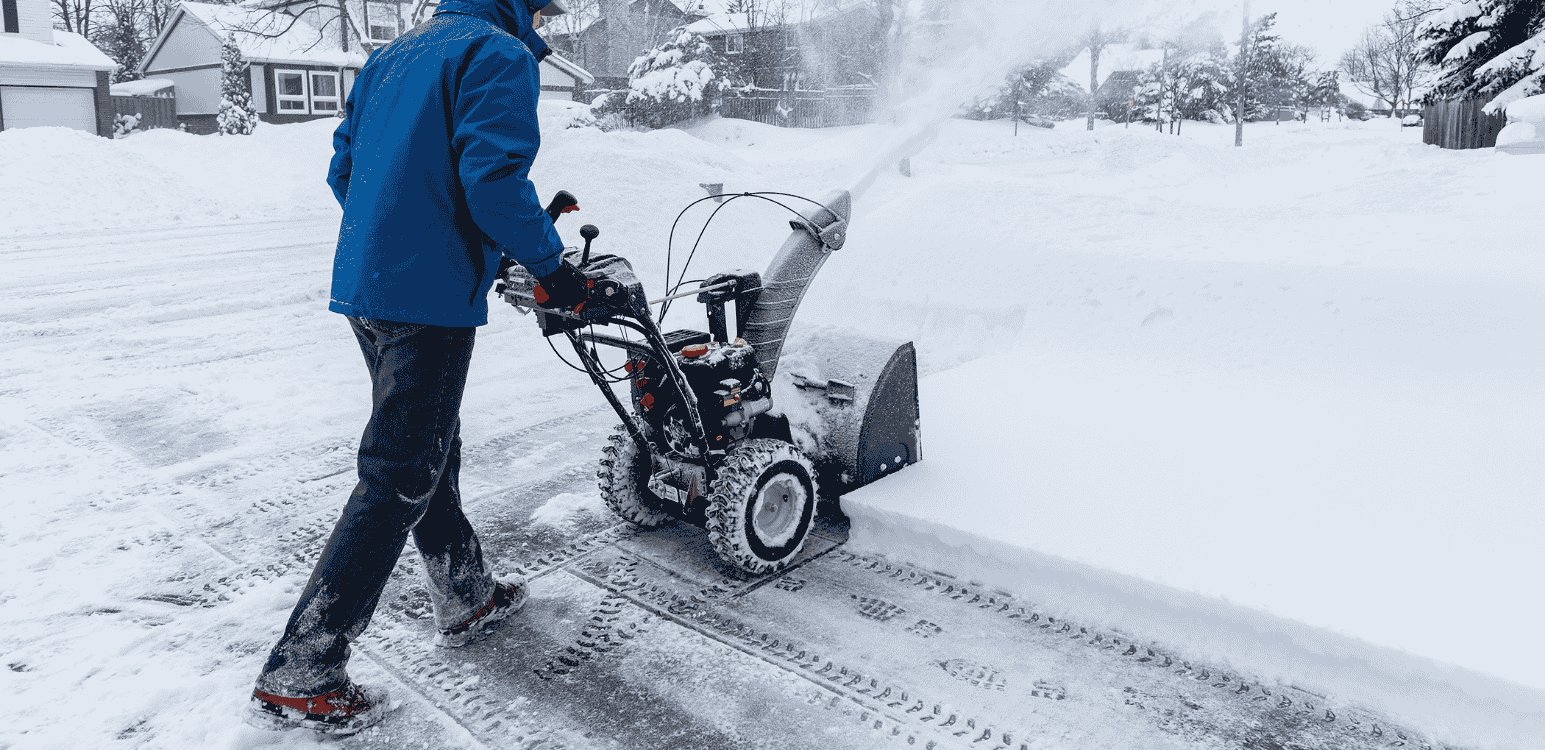 Person using a snowblower to clear heavy snow from a residential asphalt driveway.